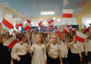 Dzieci podczas śpiewania piosenki - machają nad głowami chorągiewkami biało-czerwonymi
