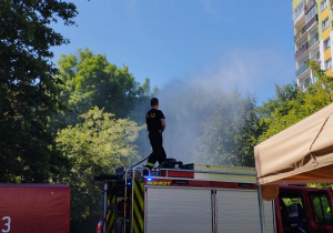 Pan Strażak stoi na wozie strażackim i rozpryskuje mgiełkę wodną na dzieci