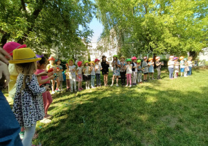 Dzieci podczas zabawy muzyczno-ruchowej - stoją ustawione w rzędzie w kolorowych kapeluszach na głowach